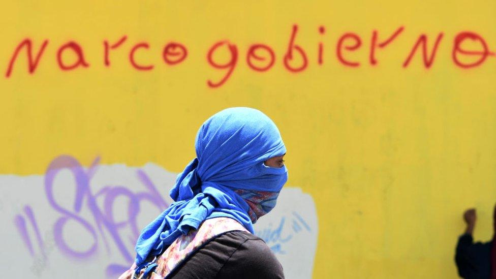 A student of the National Autonomous University of Honduras (UNAH) takes part in a protest near a wall reading "Narco-government" in Tegucigalpa on 14 August 2019