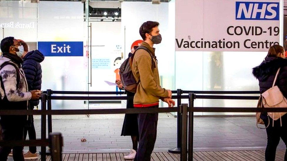 People are seen in a queue for their booster dose while standing at social distance outside the NHS vaccination centre at Westfield Stratford