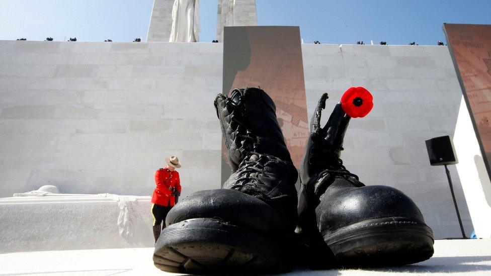 Military boots symbolising dead soldiers are seen as a Canadian police mounted officer stand guards before the ceremony to commemorate the 100th anniversary of the battle of Vimy Ridge, at Canadian National Memorial in Vimy, France, April 9, 2017