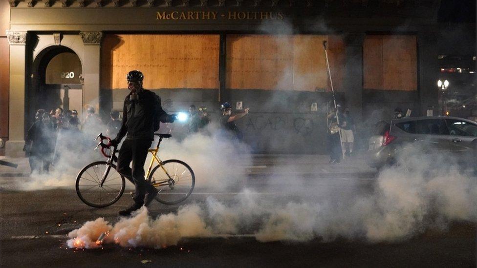 A demonstrator with a bicycle moves past a gas canister in the road near the courthouse in Portland