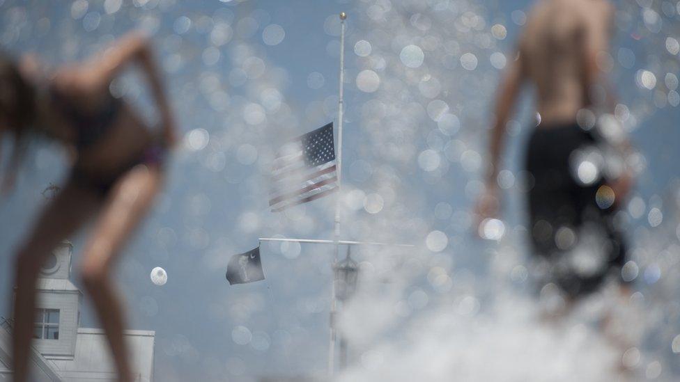 2015-06-21. An flag flew at half mast as children played in a fountain at Waterfront Park, Charleston. Colm O'Molloy for BBC News.