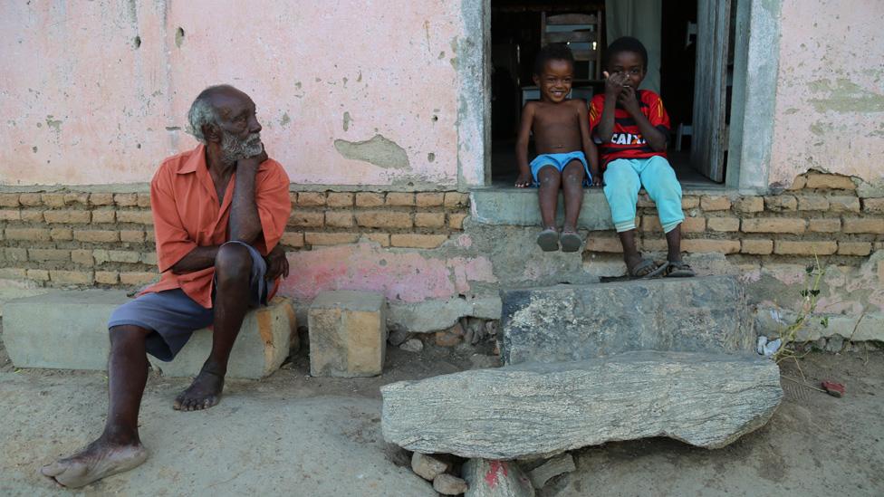 A man and two children sit on the steps of a house in Quilombo Primavera