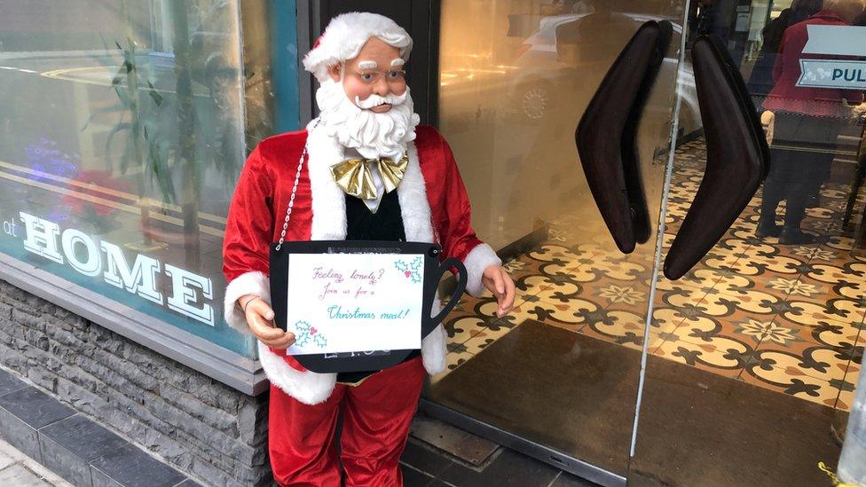 Santa holding up a sign inviting lonely people in for food