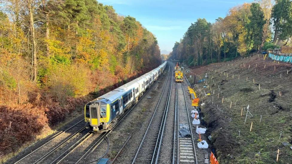 A train runs next to the landslip, with two tracks closed due to a landslip