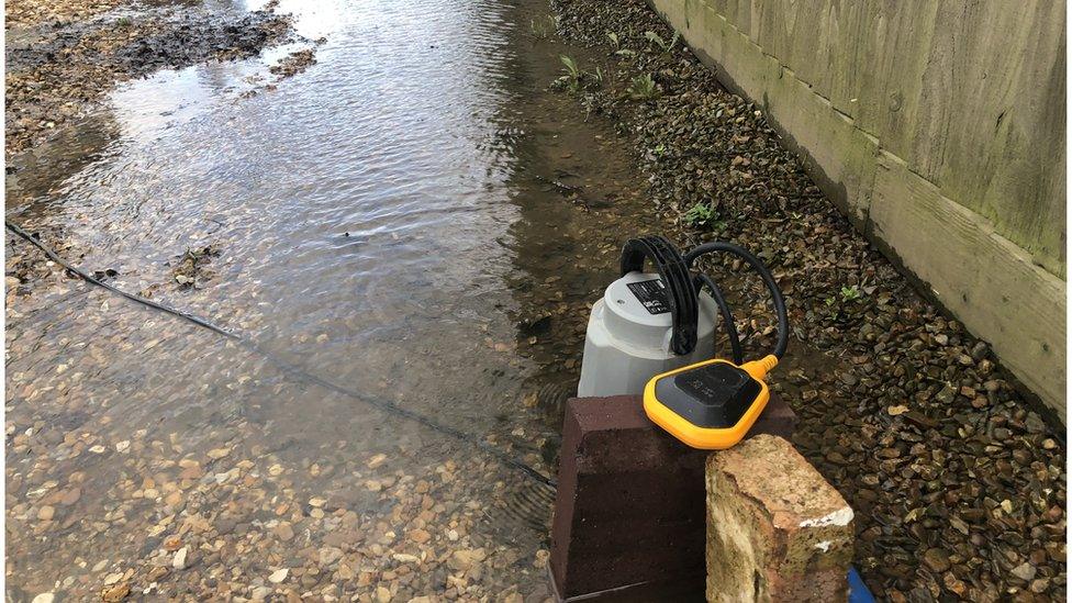 A large puddle of water, with a pump in a back garden