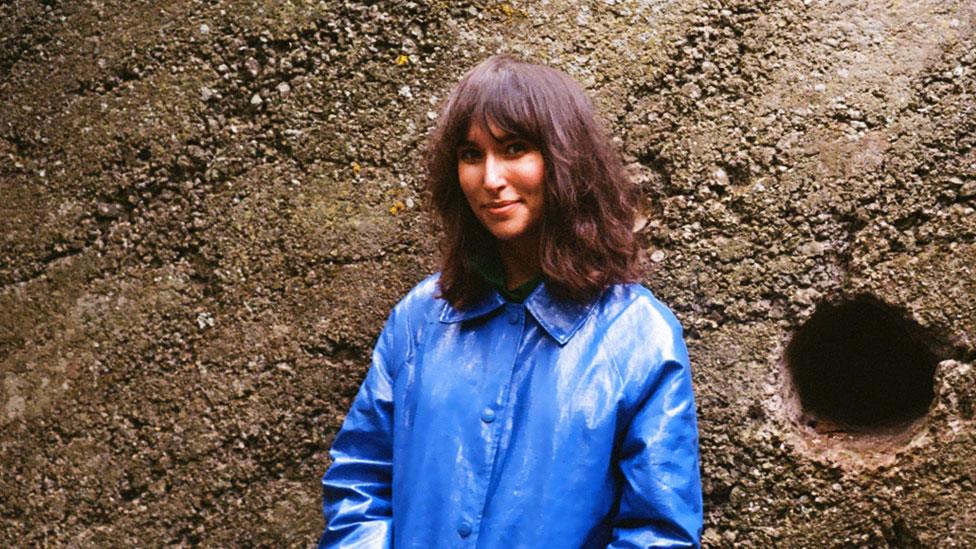 Rebecca Birell standing against a wall in a blue rain jacket