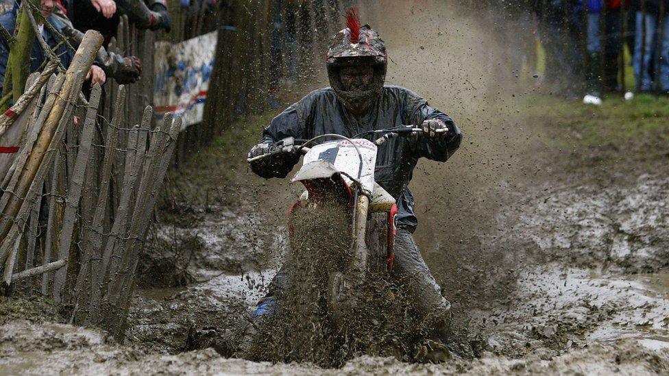 Rider soaked in mud riding a bike past spectators