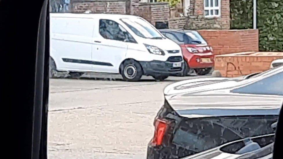 A white van with two other cars in the background