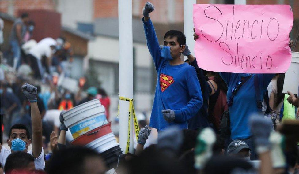 A boy in a superman t-shirt raises his fist in the gesture for silence, as rescuers look for buried victims of the quake