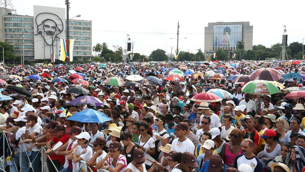 People look on as Pope Francis performs Mass