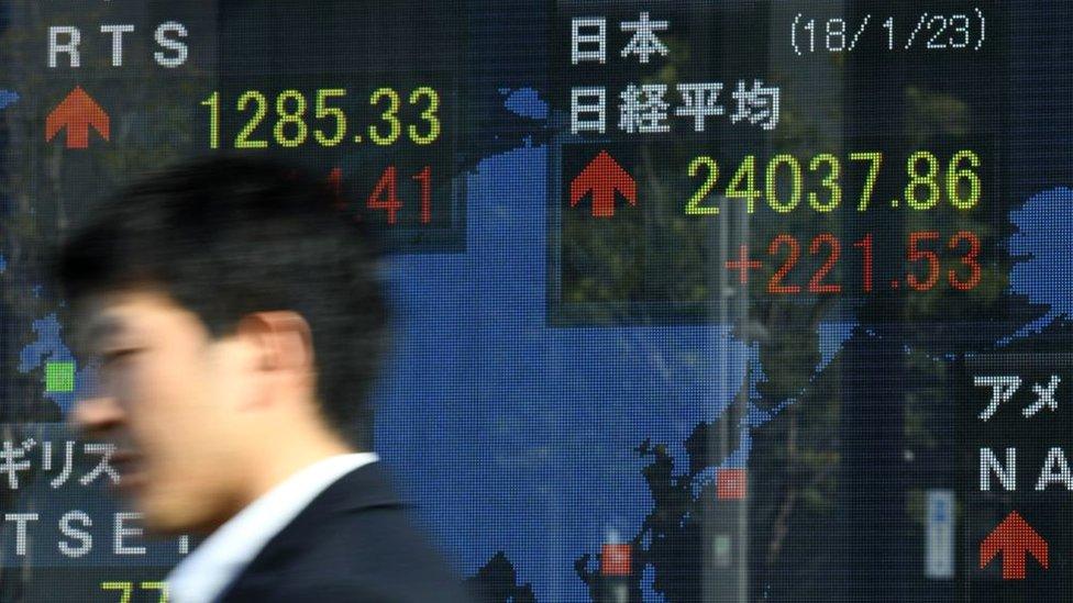 A pedestrian walks past an electronics stock indicator in the window of a securities company displaying the morning closing numbers at the Tokyo Stock Exchange in Tokyo on January 23, 2018