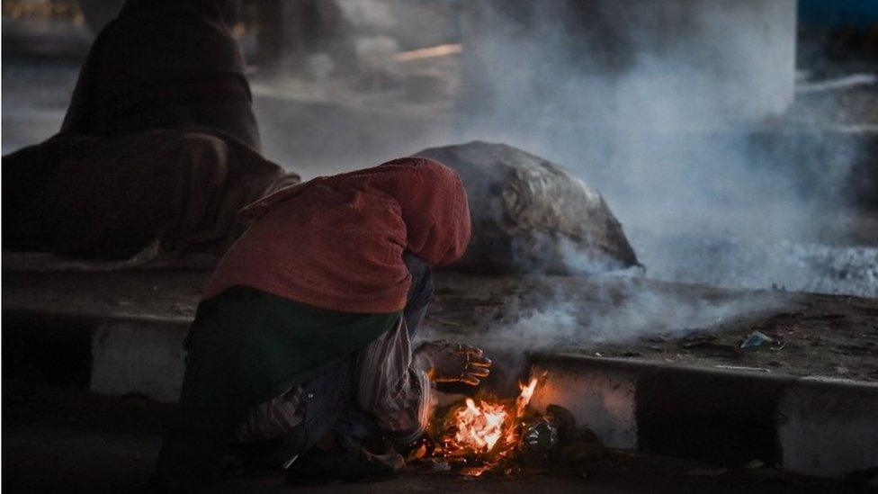 a cycle rickshaw driver curls over a fire he made from trash he found under an overpass in an effort to keep warm on a cold rainy morning in New Delhi. India's capital,