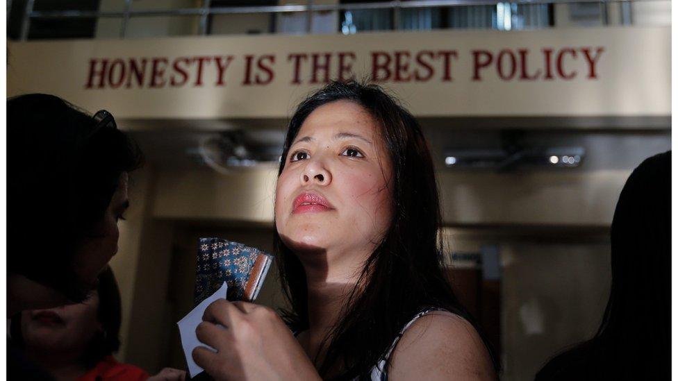 A woman's face as she stands in a queue before sunrise, to cast her vote inside a school polling station in Makati city, south of Manila. On the outside of the school is written "honesty is the best policy"