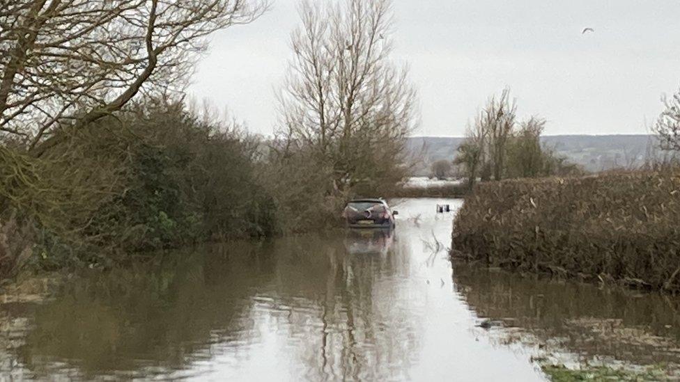 A flooded road in the Somerset levels with a stuck car