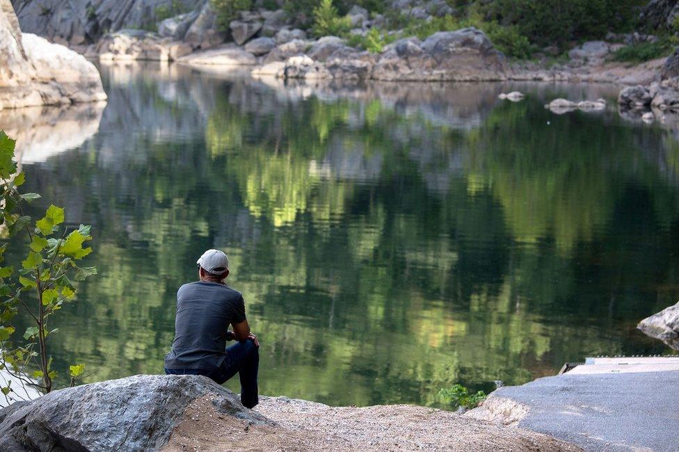 In the lower left, Barack Obama watches the reflections on the calm Potomac River, surrounded by rocks and trees.