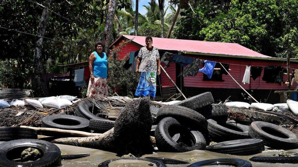 Resident Lavenia McGoon (R) with a family member standing past a makeshift seawall of old rubber car tyres to prevent erosion, outside her beachfront house at a village in the coastal town of Togoru, some 35 kilometres from Fijis capital city Suva.