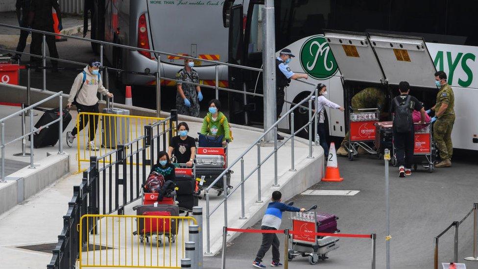 Recently returned passengers wearing face masks take their luggage to a quarantine hotel in Sydney