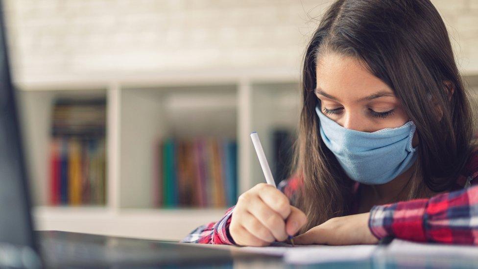 A girl wearing a mask sits at a computer and writes