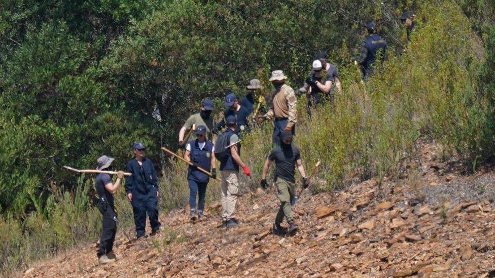 Police officers carrying digging equipment near a reservoir in Portugal