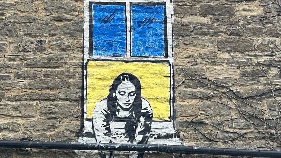 Close up of mural showing a lady in a window coloured yellow and blue like flag of Ukraine