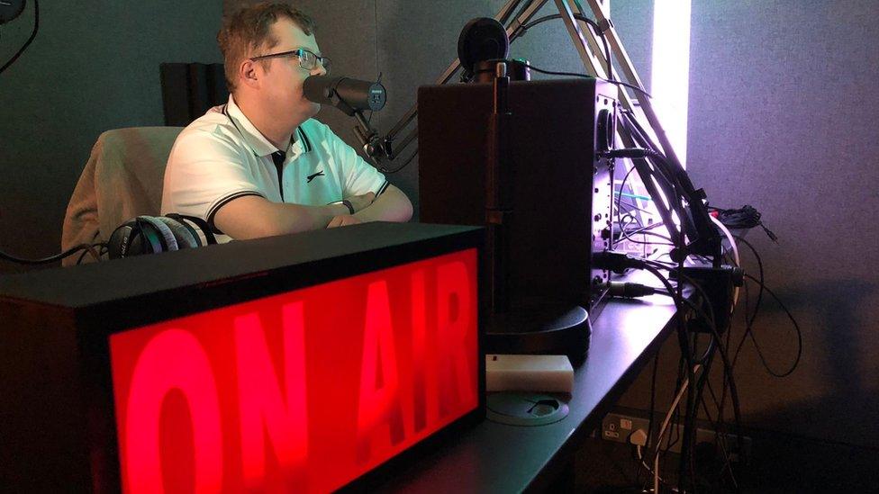 The Hub's broadcast room with a person sitting in front of a mic and a large 'ON AIR' light box in front of them