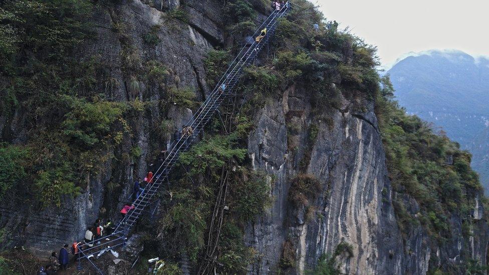 The bridal procession climb on the newly-built metal ladder with hand railings to Atuler village as the old vine ladder is seen beside it on a cliff on November 11, 2016 in Zhaojue county, China.