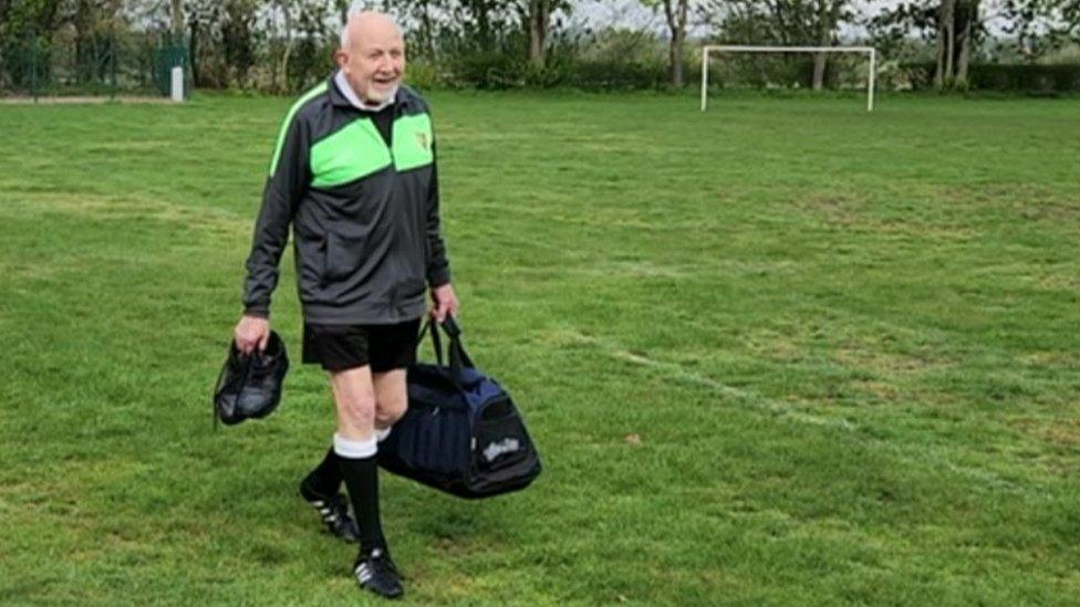 Ernie Broughton, carrying a sports holdall, arriving at a football field