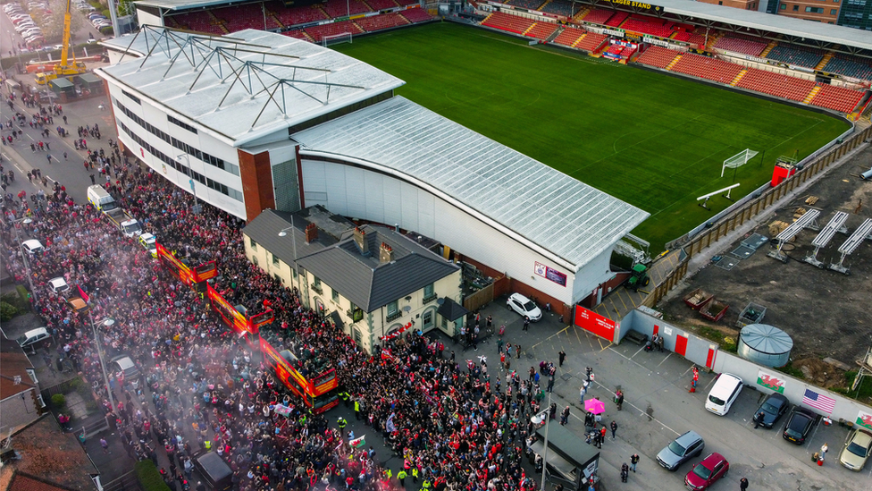 The scenes as fans gathered to greet the buses outside The Racecourse ground