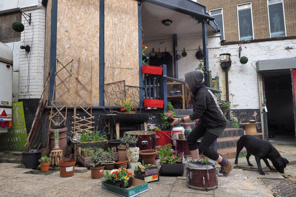 A woman and a dog outside the building surrounded by plants and garden ornaments