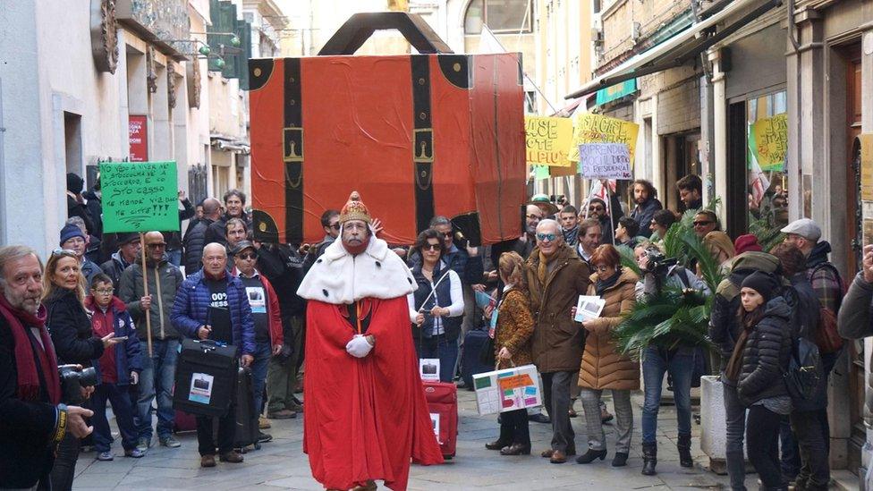 A resident dressed like the Doge of Venice walks in front of a giant luggage during the "Venexodus" demonstration.