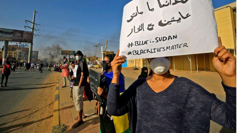 A Sudanese protester holds up a sign reading in Arabic "our martyrs are not dead, they are alive with the revolutionaries" along with the English slogans "#BLUEforSUDAN" and "#BLACKLIVESMATTER", as demonstrators mark the first anniversary of a raid on an anti-government sit-in and some demonstrate in support of US protesters over the death of George Floyd, in the Riyadh district in the east of the capital Khartoum on June 3, 2020