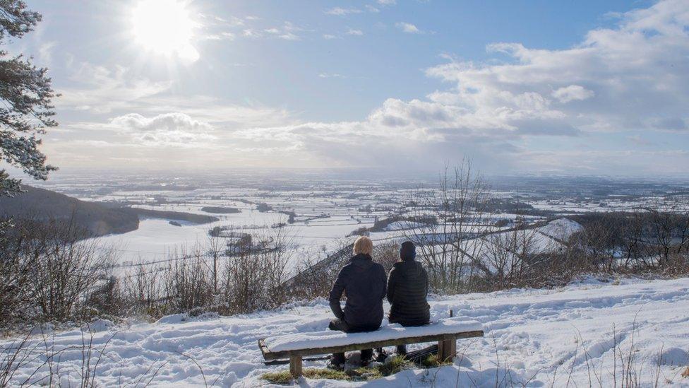 A couple sat on a bench overlooking the snow-covered fields of Thirsk at Sutton Bank National Park Centre in the North York Moors