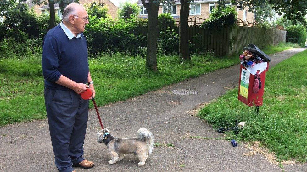 A dog walker in Northampton stares at an overflowing dog waste bin