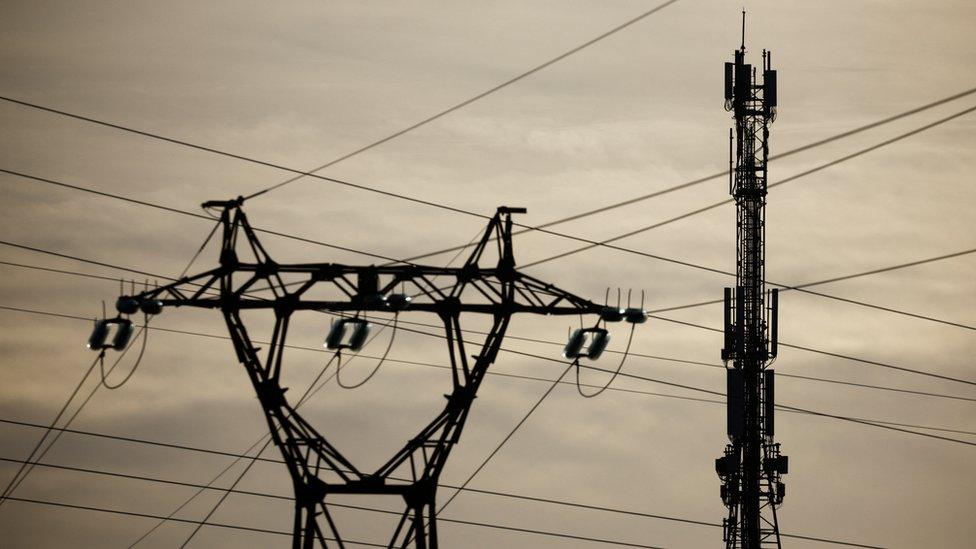 A mobile-phone relay mast is seen behind a pylon of high-tension electricity power lines