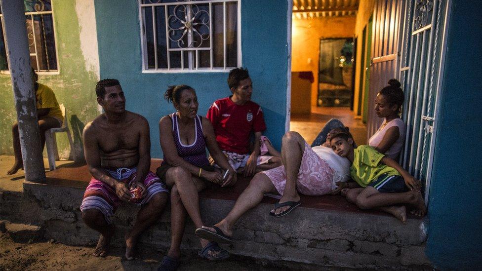 Stephanie, Diego and others sit and chat outside their front gate