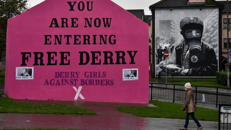 A woman walks past a mural that states "Derry Girls Against Borders" at Free Derry Corner on October 9, 2018 in Londonderry, Northern Ireland.