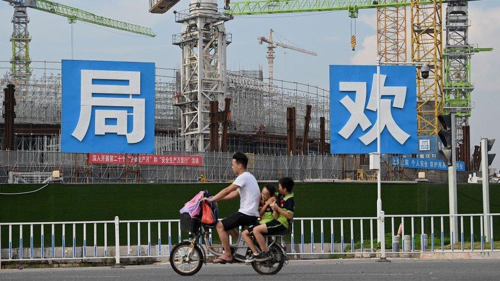 A man and children cycle past the Guangzhou FC football stadium, which is being built by Evergrande.