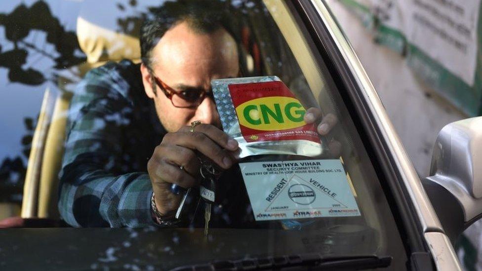 In this photograph taken on December 29, 2015, an Indian commuter puts a sticker on his vehicle that shows it runs on compressed natural gas (CNG) after getting it checked at a pump in New Delhi