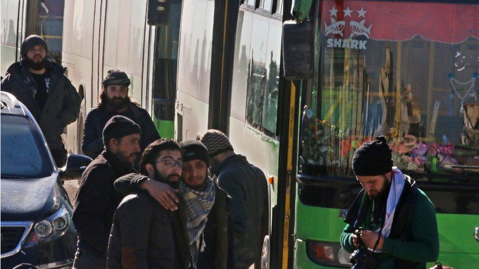 Men react as they stand outside buses evacuating people from a rebel-held sector of eastern Aleppo