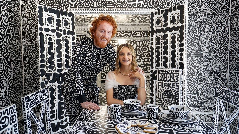 sam and alena at their dining room table covered in doodles with a box of cereal called doodle flakes sat on the table next to them