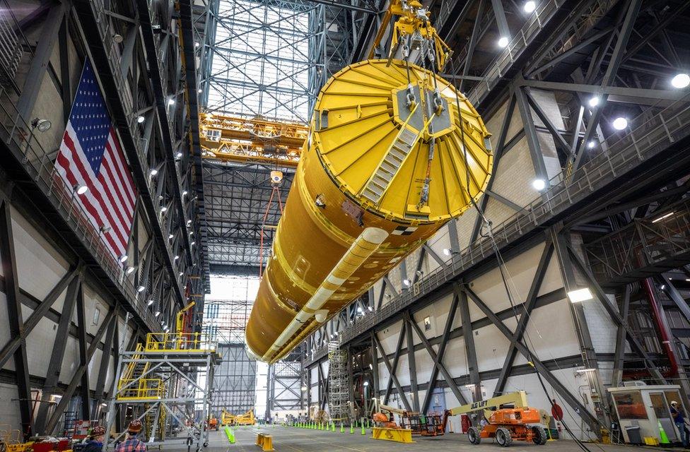 Core stage being lifted up from its position in the transfer aisle at the Vehicle Assembly Building (VAB)