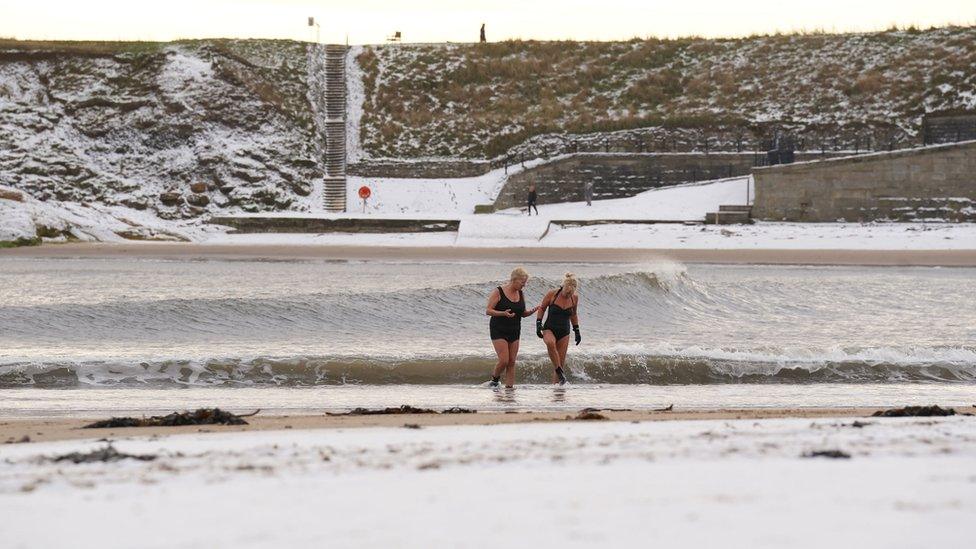 Cold-water swimmers walk across a snow-covered beach at Cullercoats Bay on the North-East coast