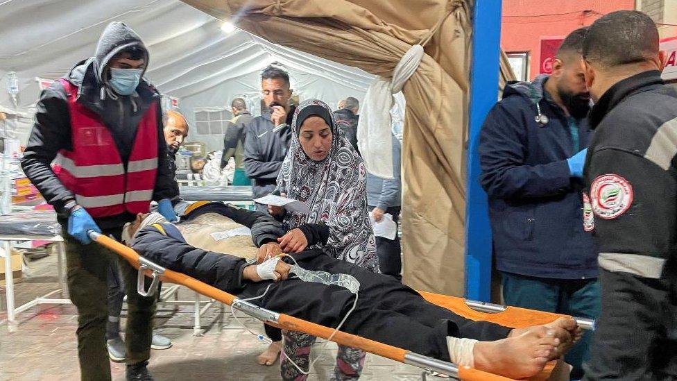 A wounded man on a stretcher is taken into a tent by medical staff