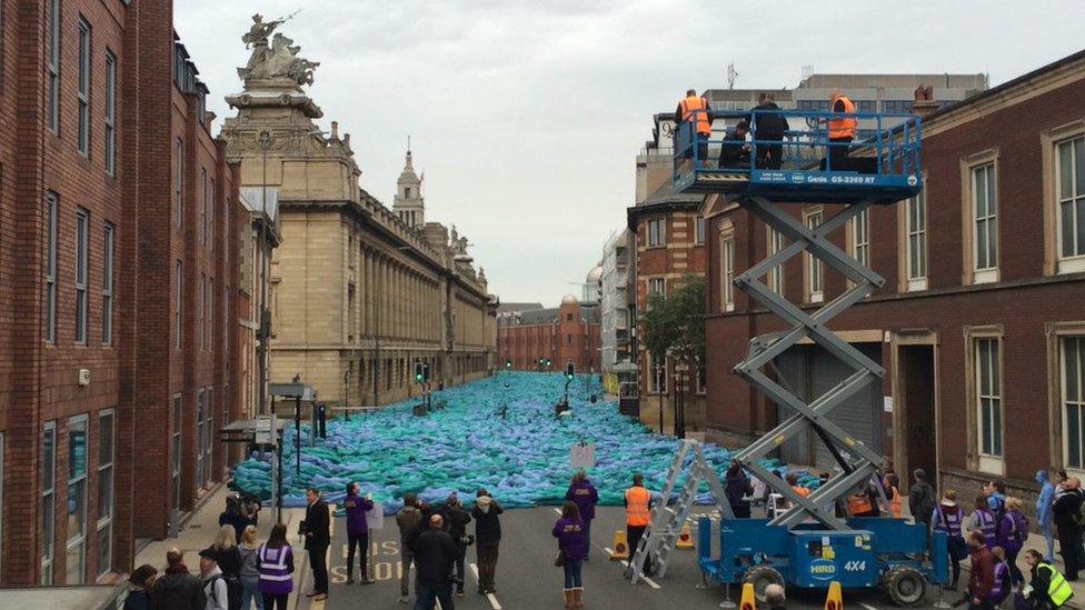 Naked people painted blue lying down on Alfred Gelder Street