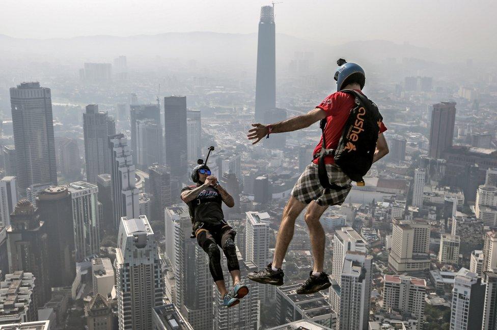 Two base jumpers jump off the edge of a tall building