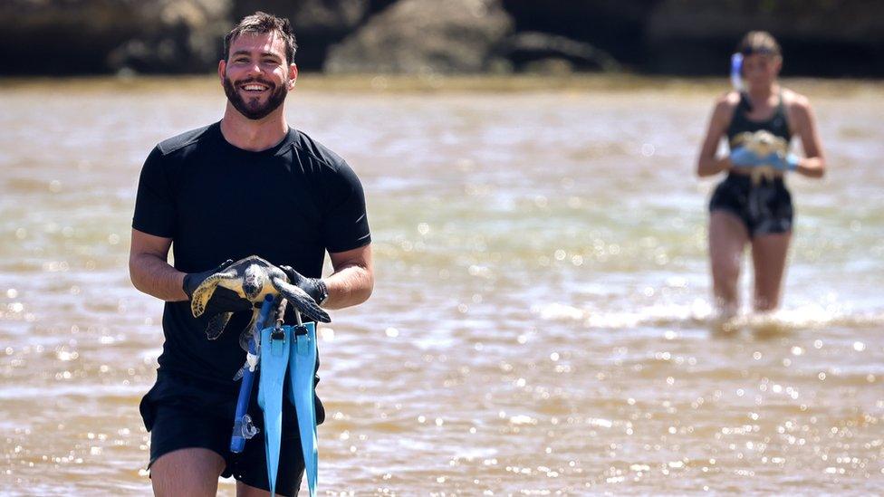 two people walk on a beach holding turtles