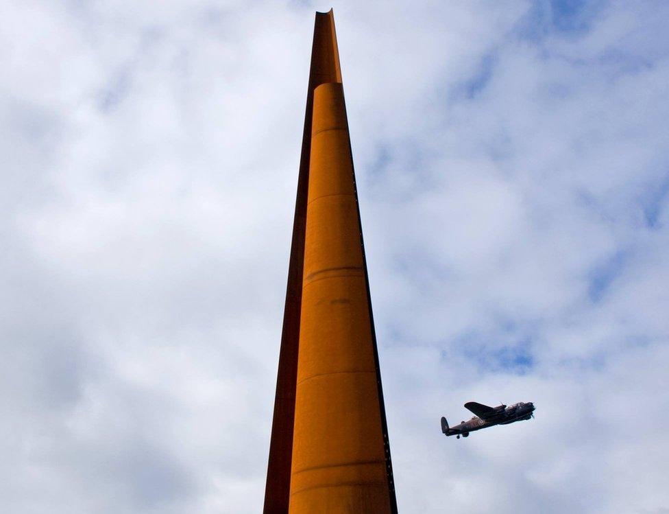 Lancaster bomber flying past memorial spire in Lincoln