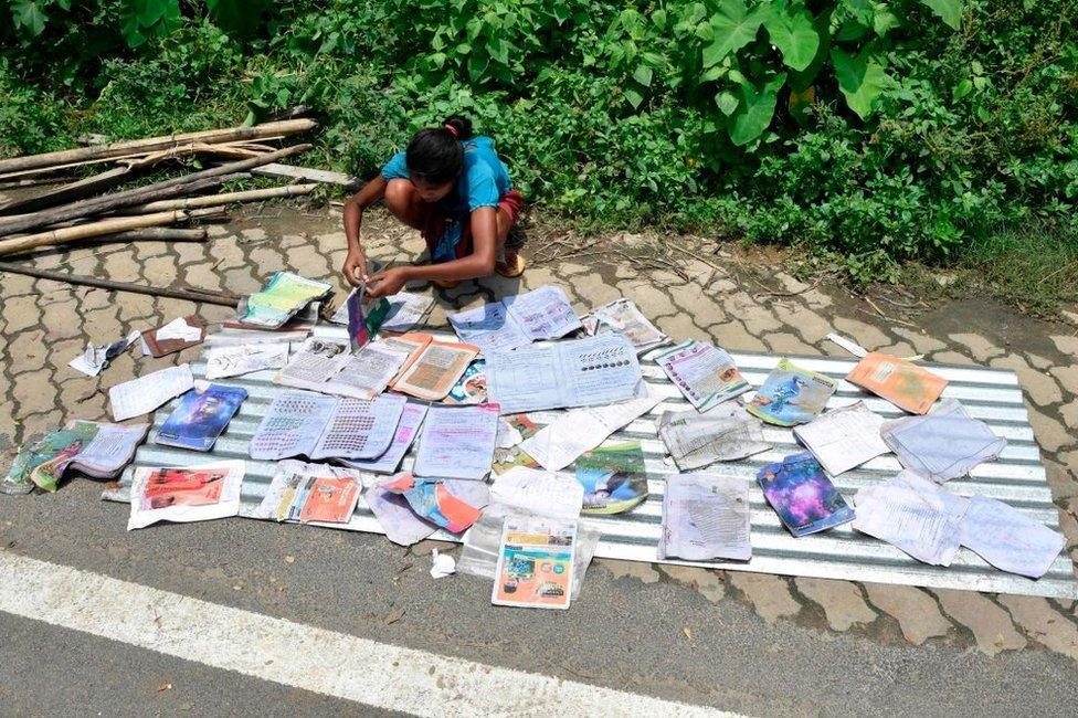 A girl places her school books to dry along a roaside at the flood affected area of Hatishila in Kamrup district of India's Assam state on July 16, 2019.