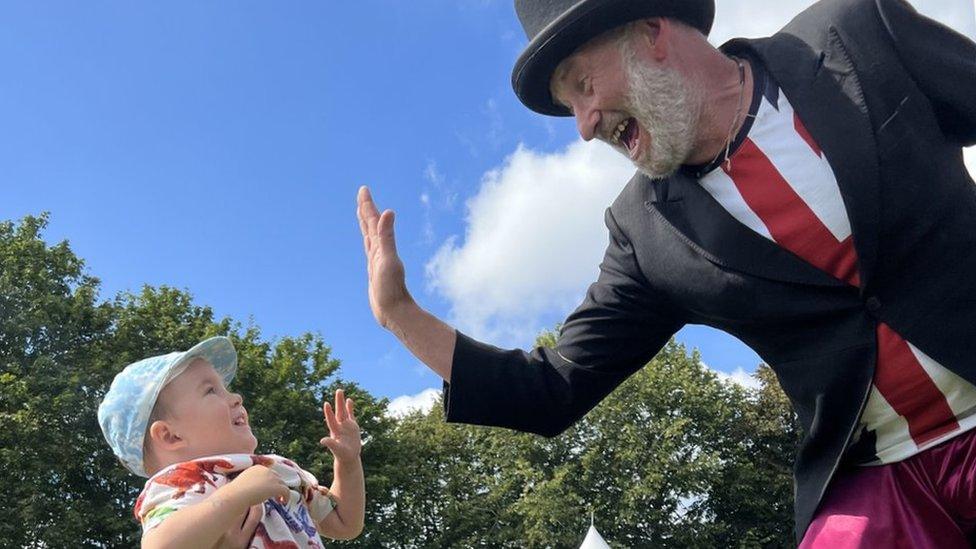 A man on stilts high-fiving a baby