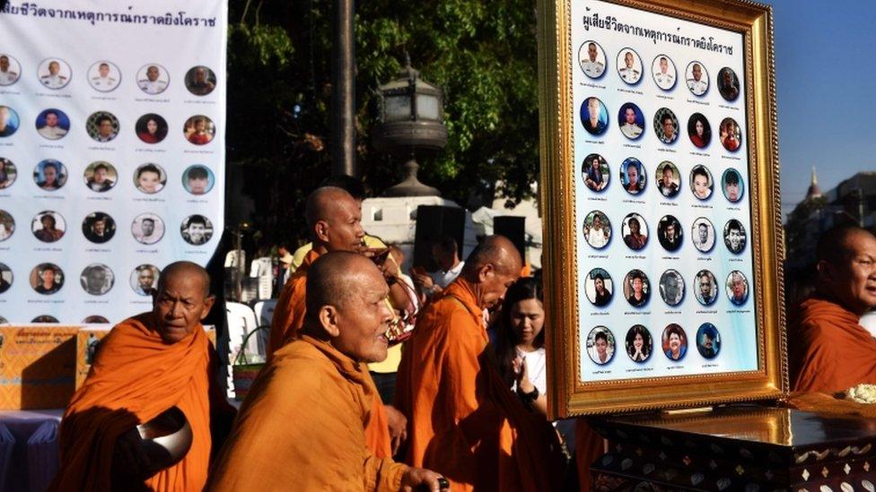 Buddhist monks walk past photographs of the victims of a mass shooting one week after a lone soldier shot and killed 29 people in Thailand